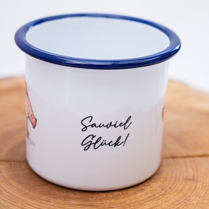May include: White enamel mug with a blue rim. The mug has a cartoon illustration of a pig and the text "Sawviel Gl&uuml;ck!" printed on the side.