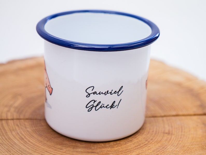 May include: White enamel mug with a blue rim. The mug has a cartoon illustration of a pig and the text "Sawviel Gl&uuml;ck!" printed on the side.