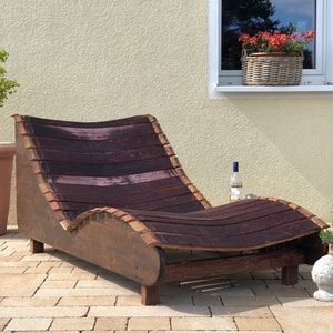 K&ouml;nnte beinhalten: Eine Chaiselongue aus Holz, hergestellt aus wiederverwendeten Weinf&auml;ssern. Die Liege ist dunkelbraun mit einem geschwungenen Design und steht auf einer Terrasse.