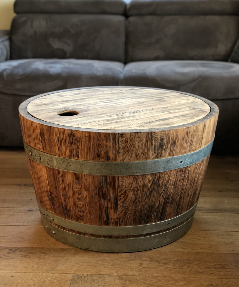 May include: A round wooden table made from a repurposed barrel with a metal band and a wooden top. The table has a small hole in the top.