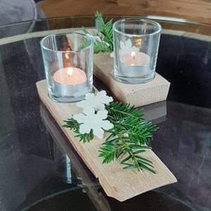 Peut inclure: Deux bougeoirs en verre avec des bougies chauffe-plat allumées sur une base en bois avec des décorations de flocons de neige blancs et des brins de pin verts.
