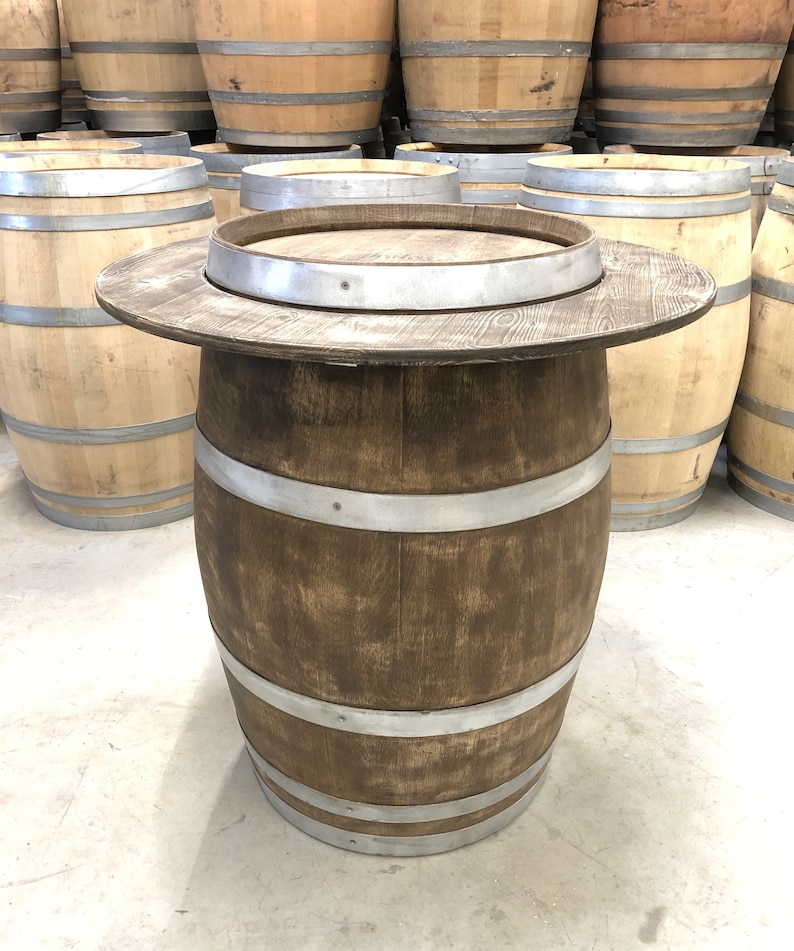 May include: A wooden barrel table with a brown stain and silver metal bands. The table top is made of wood and has a round shape.