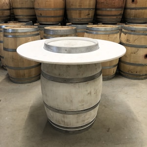 May include: White painted wooden barrel with a white round tabletop. The barrel is used as a table and has metal bands around it.