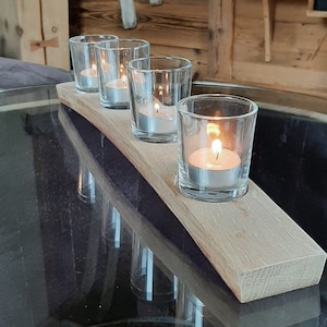 Può includere: Un portacandele in legno con quattro portacandele in vetro, ognuno con una candela tea light accesa. Il portacandele è realizzato in un pezzo di legno con una finitura naturale.