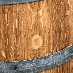 May include: A wooden barrel with a metal band around the top and bottom. The wood is a light brown colour and has a natural grain pattern. The metal band is a silver colour and has a slightly weathered look.