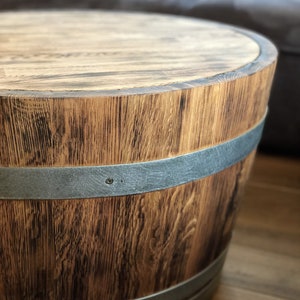 May include: A wooden barrel table with a dark brown stain and two silver metal bands around the top and bottom. The table has a round top and a slightly flared base.
