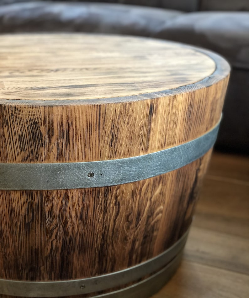 May include: A wooden barrel table with a dark brown stain and two silver metal bands around the top and bottom. The table has a round top and a slightly flared base.