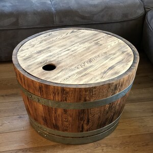 May include: A round wooden table made from a repurposed barrel with metal bands. The table has a wooden top with a small hole in the center.