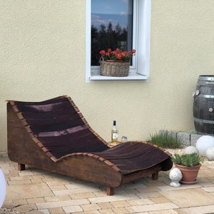 K&ouml;nnte beinhalten: Ein Holz-Liegestuhl aus wiederverwendeten Weinf&auml;ssern. Der Stuhl ist braun mit einem dunkelbraunen Streifenmuster und steht auf einer Terrasse mit einem Fass und Topfpflanzen.
