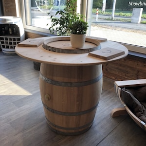 May include: A wooden barrel table with a round top and a natural wood finish. The table has a metal band around the barrel and two wooden serving trays on top. A small potted plant sits on the table.