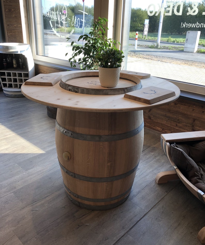 May include: A wooden barrel table with a round top and a natural wood finish. The table has a metal band around the barrel and two wooden serving trays on top. A small potted plant sits on the table.