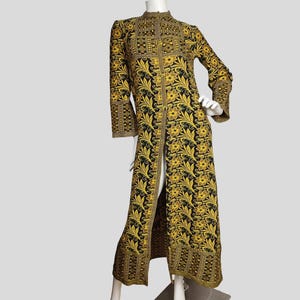 May include: A long, black and gold embroidered coat with a floral design. The coat has a high collar, long sleeves, and a front split. The garment is displayed on a mannequin.