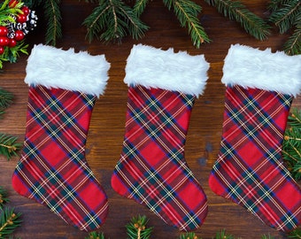 May include: Three red and green plaid Christmas stockings with white faux fur trim. The stockings are hanging on a wooden surface.