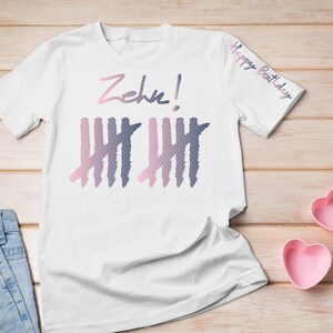 Könnte beinhalten: Weißes T-Shirt mit dem Text "Zehn!" und einer Grafik von zehn Zählstrichen in Rosa und Blau. Der Text "Happy Birthday" befindet sich auf dem Ärmel.