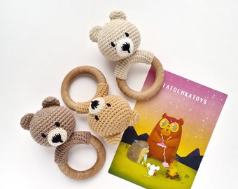 Puede incluir: Tres juguetes de sonajero de oso de crochet con anillos de madera. Los osos son marrones y beige. Los osos están sobre una superficie blanca con una tarjeta que dice "TatochkaToys".