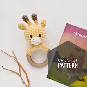 May include: A crocheted giraffe rattle with a wooden ring. The giraffe is yellow with brown spots and has a white face. The rattle is a great toy for babies.