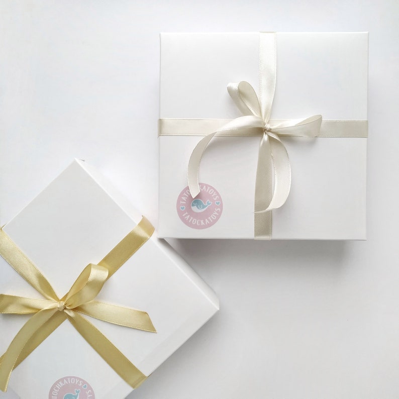 May include: Two white gift boxes with gold and ivory ribbon bows. The boxes are tied with ribbon and have a sticker with a whale design and the text "Little Toys Tatoockairy's".