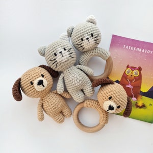 May include: Four crocheted animal toys, two gray cats and two brown dogs, with wooden teething rings. The toys are arranged on a white surface with a book titled "TatochkaToy" in the background.
