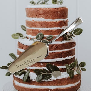 Könnte beinhalten: Eine zweistöckige Hochzeitstorte, verziert mit Grünpflanzen und einem personalisierten Tortenmesser. Das Messer ist mit "Lea & Simon 12.05.2024" graviert.