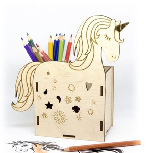 May include: Wooden unicorn pencil holder with a gold horn and a cutout design of flowers and stars. The holder is filled with colored pencils.