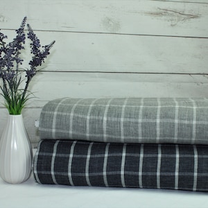 Könnte beinhalten: Zwei Rollen Stoff mit kariertem Muster. Die obere Rolle ist ein hellgrauer Stoff mit weißen Karos. Die untere Rolle ist ein dunkelgrauer Stoff mit weißen Karos.