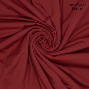 Könnte beinhalten: Nahaufnahme einer Wirbel aus tiefrotem Stoff. Der Stoff ist glatt und scheint eine einfarbige Farbe zu haben. Die Worte "Fibre Good Fabrics" befinden sich in der oberen rechten Ecke.