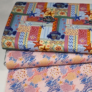 Könnte beinhalten: Drei Stoffrollen mit maritimen Mustern. Die obere Rolle zeigt ein Patchwork-Design mit Fischen, Seesternen und Schildkröten in Blau-, Orange- und Rottönen. Die unteren Rollen zeigen ein rosa-blaues Meeresleben-Muster.
