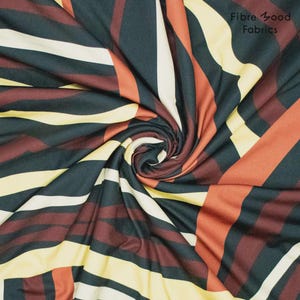 Könnte beinhalten: Nahaufnahme eines Stoffes mit geometrischem Muster. Der Stoff weist einen Wirbel aus diagonalen Streifen in Schwarz, Creme, Gelb und Rotbraun auf. Der Text "Fibre Good Fabrics" ist in der oberen rechten Ecke sichtbar.