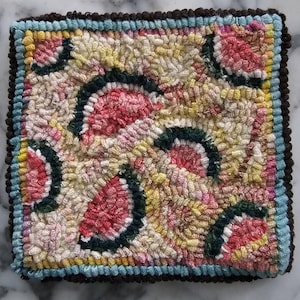 May include: A square punch needle textile featuring a repeating pattern of stylized watermelon slices in pink, dark green, and cream. The piece is bordered by a light blue frame and a dark brown outer edge, showcasing a textured, looped yarn finish.