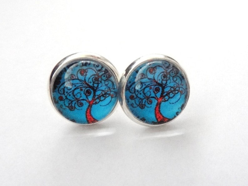 May include: A pair of silver stud earrings with a blue and red tree of life design.