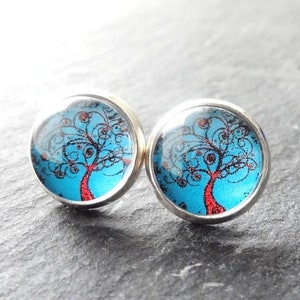 Könnte beinhalten: Ein Paar silberne Ohrstecker mit blauem Hintergrund und einem roten Baum mit schwarzen Spiralen.