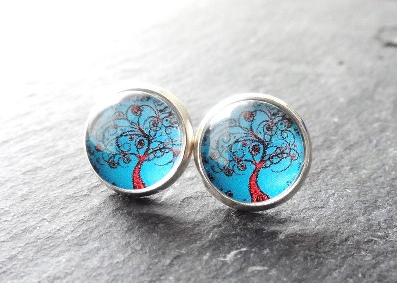 May include: A pair of silver stud earrings with a blue background and a red tree with black swirls.