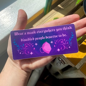 May include: A rectangular sticker with a purple background and the text "Wear a mask everywhere you think disabled people deserve to be." The sticker has decorative floral and star elements, and a pink mask graphic.