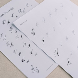 May include: Two sheets of paper with cursive alphabet practice sheets. The top sheet shows the letters A through Z in cursive script. The bottom sheet shows the letters G and H in cursive script.