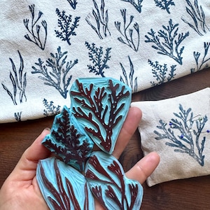 May include: Handmade linoleum stamps with a marine theme. The stamps are blue and brown, depicting seaweed and coral. A matching fabric with printed seaweed patterns and a small printed pillow are also visible.