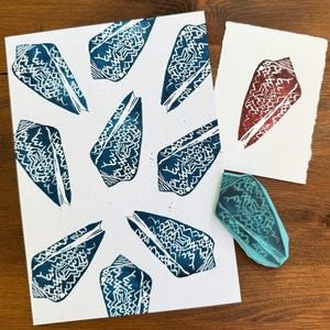 Può includere: Una carta bianca con più stampe di conchiglie verde acqua. Una carta più piccola presenta una stampa di conchiglia rossa. È visibile anche un timbro di conchiglia verde acqua. Le stampe di conchiglie hanno intricati motivi bianchi.