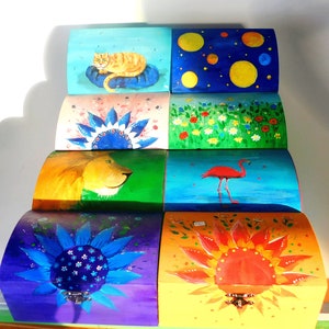 May include: Set of seven colourful wooden boxes with hand-painted designs. The boxes feature a cat, a lion, a flamingo, a sunflower, a daisy, a starry night sky, and a field of flowers.