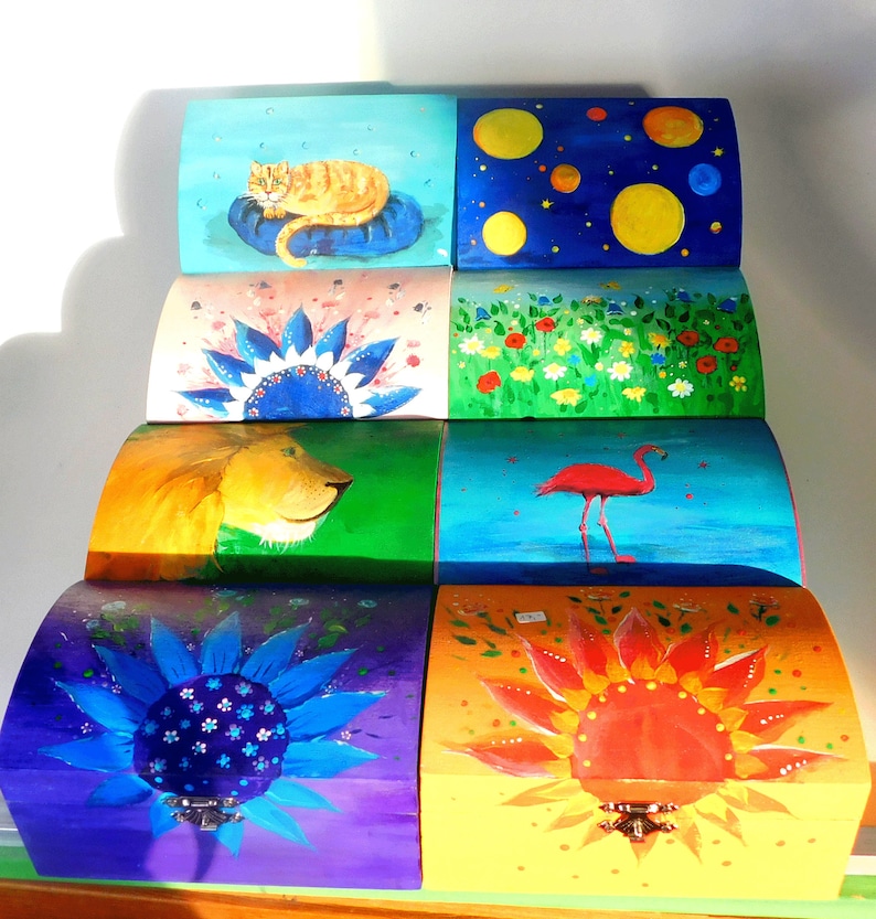 May include: Set of seven colourful wooden boxes with hand-painted designs. The boxes feature a cat, a lion, a flamingo, a sunflower, a daisy, a starry night sky, and a field of flowers.