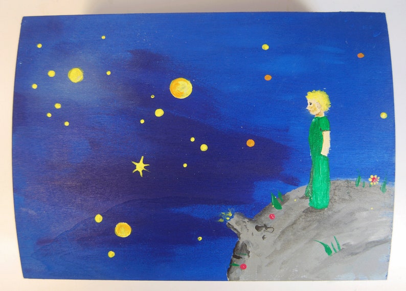 May include: A hand-painted wooden box with a blue night sky background. The box features a yellow star, a yellow crescent moon, and a small figure of a person standing on a grey rock. The figure is wearing a green shirt and trousers.