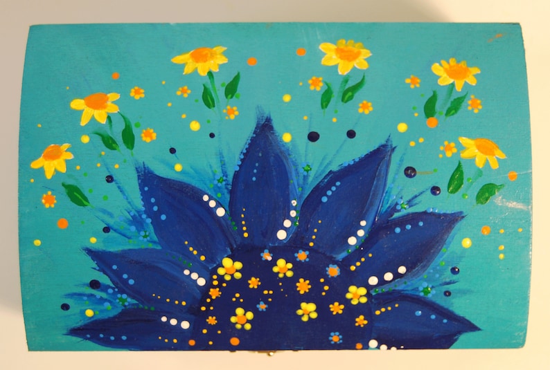 May include: A blue and yellow painted wooden box with a sunflower design. The sunflower has a blue centre with yellow petals and white dots. The background is turquoise with yellow flowers and orange dots.