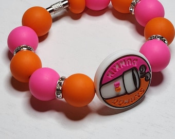 May include: A beaded bracelet featuring alternating pink and orange beads, with silver rhinestone accents. The bracelet includes a charm with the Dunkin' Donuts logo. The bracelet is secured with a silver clasp.