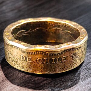 以下が含まれることがあります： チリのコインで作られた金色のリング。リングには「DE CHILE」という文字が刻まれています。