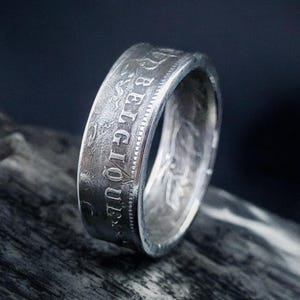Può includere: Un anello d'argento realizzato con una moneta belga. L'anello presenta l'iscrizione "BELGIQUE" sul lato.