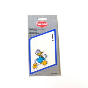 May include: A white card with blue and red text that reads "Application zum Aufbügeln iron on motif motifs brodés thermocollants" and a Disney logo. The card features a cartoon image of Donald Duck walking.