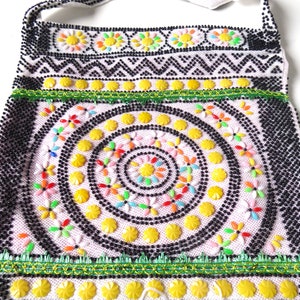 K&ouml;nnte beinhalten: Eine wei&szlig;e Perlenhandtasche mit einem schwarz-wei&szlig;en geometrischen Muster, einem gr&uuml;n-gelben Besatz und einem kreisf&ouml;rmigen Design aus gelben, rosa und mehrfarbigen Perlen.