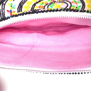 K&ouml;nnte beinhalten: Eine wei&szlig;e Perlenhandtasche mit einem rosa Stofffutter. Die Tasche hat einen Rei&szlig;verschluss und ist mit bunten Perlen verziert.