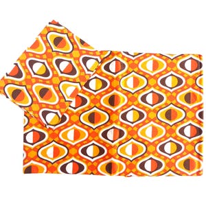 May include: Two pieces of fabric with a repeating geometric pattern in orange, brown, yellow, and white. The design features oval shapes within a diamond grid. The fabric is likely for home decor or crafting.
