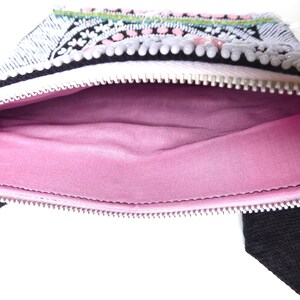K&ouml;nnte beinhalten: Eine kleine, wei&szlig;e Rei&szlig;verschlusstasche mit einem rosa Stofffutter. Die Tasche ist mit schwarzen und wei&szlig;en Perlen und rosa und wei&szlig;en Pailletten verziert.