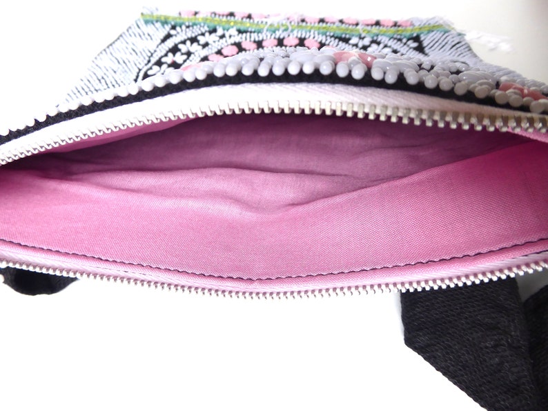 K&ouml;nnte beinhalten: Eine kleine, wei&szlig;e Rei&szlig;verschlusstasche mit einem rosa Stofffutter. Die Tasche ist mit schwarzen und wei&szlig;en Perlen und rosa und wei&szlig;en Pailletten verziert.