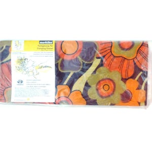 May include: A camping towel with a floral pattern, packaged in clear plastic. The design features large orange, green, and yellow flowers on a dark purple backdrop. The packaging includes text and a logo.